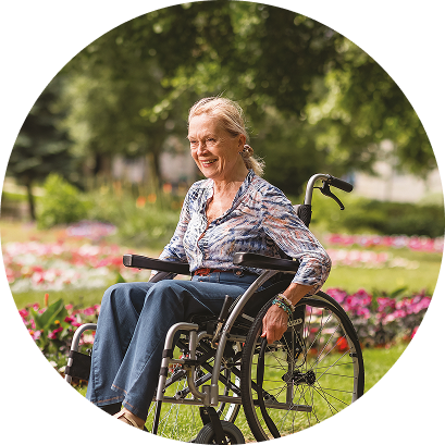 Smiling older woman sitting in a wheelchair outdoors in a park with flowers