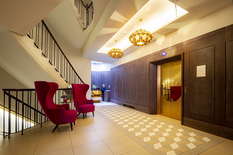 The lobby area of a traditional red brock apartment building in London with two large red wing chairs
