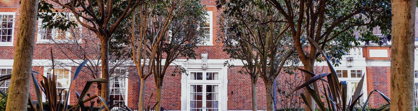 Part of a red brick apartment building through some trees