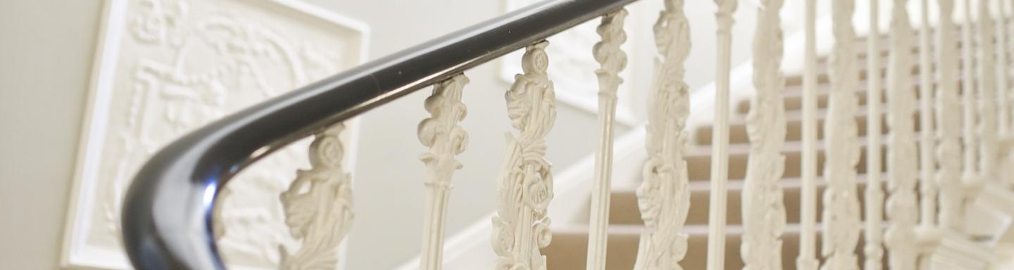 An internal staircase with cream carpets, cream balustrade and wooden banister