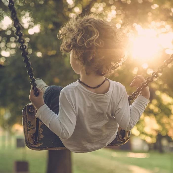 A photo of a child on a swing taken from behind with trees visible in the background